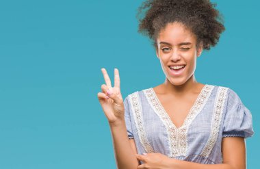 Mutlu yüz zafer işareti yaparken kameraya göz kırpıyor ile gülümseyen izole arka plan üzerinde genç afro Amerikalı kadın. İki numaralı.
