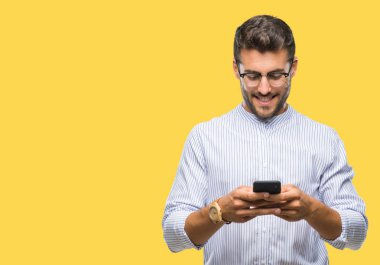 Yakışıklı delikanlı manifatura Smartphone izole arka plan üzerinde duran ve diş gösterilen kendine güvenen bir gülümsemeyle gülümseyerek mutlu bir yüz ile kullanma