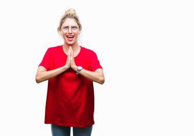 Yalvarıyor ve umut ifade yüzünde çok duygusal ve endişe ile birlikte elleriyle dua izole arka plan üzerinde kırmızı t-shirt ve gözlük giyen genç güzel sarışın kadın. Bağışlanmak. Din kavramı.