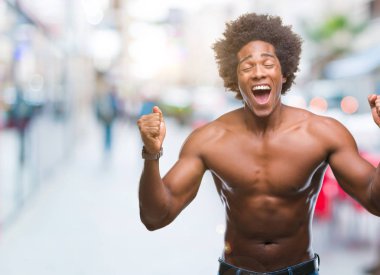 Kızgın ve çığlık kaldırdı ve kapalı gözleri heyecanlı silah ile başarı için çılgın çıplak vücut kutluyor izole arka plan üzerinde gösterilen Afro Amerikalı gömleksiz adam. Kazanan kavramı