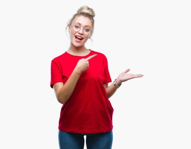 Hayret ve el ile sunulması ve parmak ile işaret ederken kameraya gülümseyen izole arka plan üzerinde gözlüklü sarışın genç kadın.