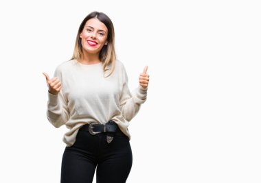 Genç güzel kadın rahat beyaz kazak üzerinde el ile pozitif jest yapıyor izole arka plan başarı işareti başparmak gülümseyen ve mutlu. Neşeli bir ifadeyle, kazanan jest kameraya bakıyor.