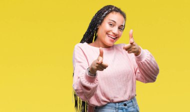 Genç örgülü saç Afro-Amerikan kız kameraya mutlu ve komik suratla parmakları işaret izole arka plan üzerinde kazak giyiyor. İyi enerji ve vibes.