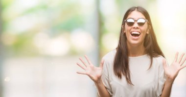 Kocaman bir gülümseme ile çığlık zaferini kutluyor ve ellerini kaldırdı genç güzel İspanyol giyen güneş gözlüğü çok mutlu ve heyecanlı, kazanan ifade