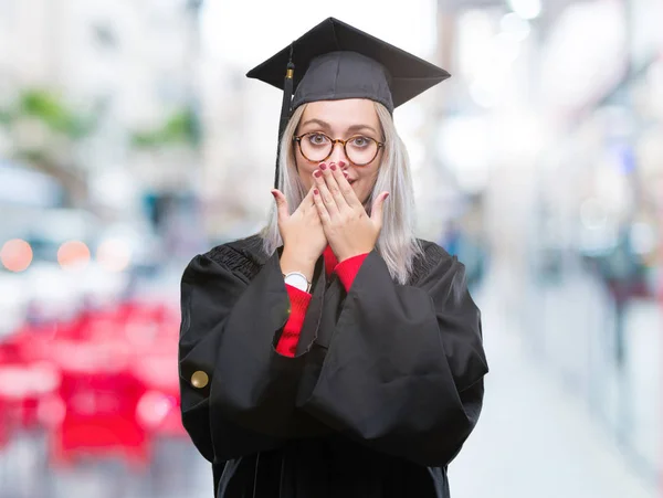 若いブロンドの女性は分離背景のミスのための手で口を覆っているショックを受けた大学院の制服を着ています 秘密の概念 — ストック写真