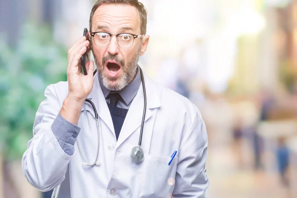 中年资深医生人谈论智能手机在孤立的背景下吓坏了惊讶的脸 害怕和兴奋与恐惧的表情 — 图库照片