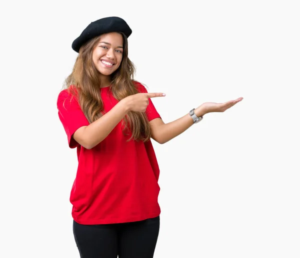 年轻美丽的黑发时尚女人穿着红色的 T恤和黑色贝雷帽在孤立的背景惊讶和微笑的镜头 同时提出与手和手指指着 — 图库照片