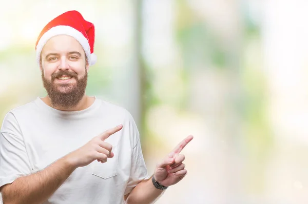 笑顔で側に つの手と指で指しているカメラを見て孤立の背景にクリスマスの帽子をかぶって若い白人ヒップ男 — ストック写真