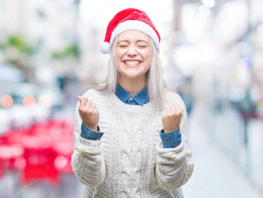 Young blonde woman wearing christmas hat over isolated background very happy and excited doing winner gesture with arms raised, smiling and screaming for success. Celebration concept.