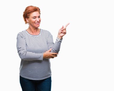 Yüzünde kocaman bir gülümseme ile izole arka plan Atrractive üst düzey beyaz Kızıl saçlı kadın kameraya bakarak yan el ve parmak ile işaret.