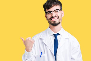 Seyir ve başparmak yanında yukarıyı mutlu yüz ile gülümseyen izole arka plan üzerinde beyaz önlük giyen genç profesyonel bilim adamı.