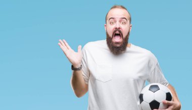 Genç beyaz hipster adam futbol futbol topu tutan kocaman bir gülümseme ile çığlık zaferini kutluyor arka plan çok mutlu ve heyecanlı, kazanan ifade izole ve ellerini kaldırdı