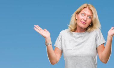 Orta yaş sarışın kadın izole arka plan clueless ve şaşkın bir ifadeyle kollar ve eller kaldırdı. Şüphe kavramı.