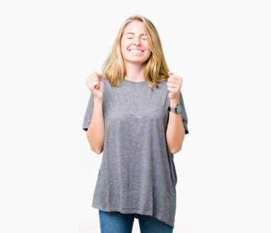 Güzel genç kadın giyiyor büyük boy rahat t-shirt izole arka plan üzerine silah ile başarı için heyecanlı zafer kutluyor gülümseyen kaldırdı. Kazanan kavramı.