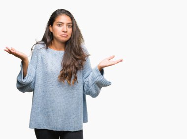 İzole arka plan clueless ve şaşkın bir ifadeyle kollar ve eller kaldırdı üzerinde kış kazak giyen genç güzel Arap kadın. Şüphe kavramı.