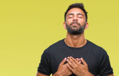 Göğüs kapalı gözler ve yüzünde minnettar jest ile yetişkin İspanyol adam ile gülümseyen izole arka plan üzerinde eller. Sağlık kavramı.