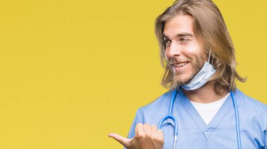 Seyir ve başparmak yanında yukarıyı mutlu yüz ile gülümseyen izole arka plan üzerinde uzun saçlı Genç yakışıklı Doktor adam.