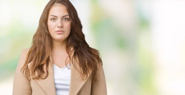 Artı boyutu genç kadın güzel üzerinde kış palto giyiyor arka plan gevşek yüzünde ciddi bir ifade ile izole. Basit ve doğal kameraya bakıyor.