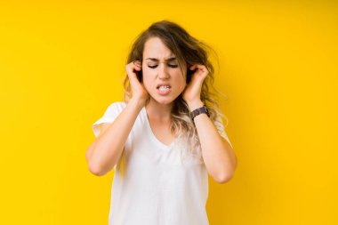 Genç güzel sarışın kadın parmakları ile yüksek sesle müzik gürültü rahatsız ifade kulaklarıyla kapsayan sarı arka plan yüzünden. Sağır kavramı.