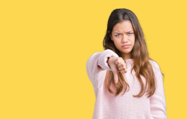 Mutsuz ve kızgın ret gösterilen ve başparmak aşağı hareketi ile negatif seyir izole arka plan üzerinde pembe kış kazak giyen genç güzel esmer kadın. Kötü ifade.