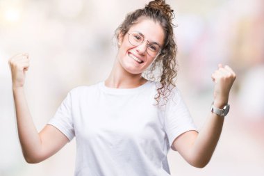 Esmer kıvırcık saçlı kız izole arka plan üzerinde kutluyor gözlük takan şaşırttı ve silah ile başarı için hayran güzel genç kaldırdı ve gözleri açık. Kazanan kavramı.