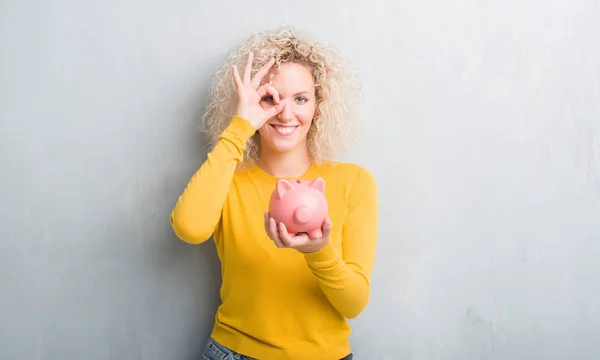 Young Blonde Woman Grunge Grey Background Holding Piggy Bank Happy — Stock Photo, Image