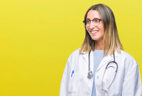 Young beautiful doctor woman headphones over isolated background looking away to side with smile on face, natural expression. Laughing confident.