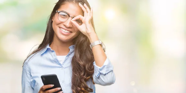 年轻美丽的阿拉伯妇女发短信使用智能手机在孤立的背景下 快乐的脸微笑做 标志与手在眼睛看通过手指 — 图库照片