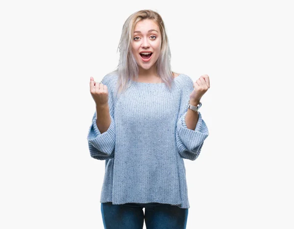 孤立した背景を祝う上冬のセーターを着ている若いブロンドの女性驚いて腕を上げると成功のため驚くし 目を開きます 勝者の概念 — ストック写真
