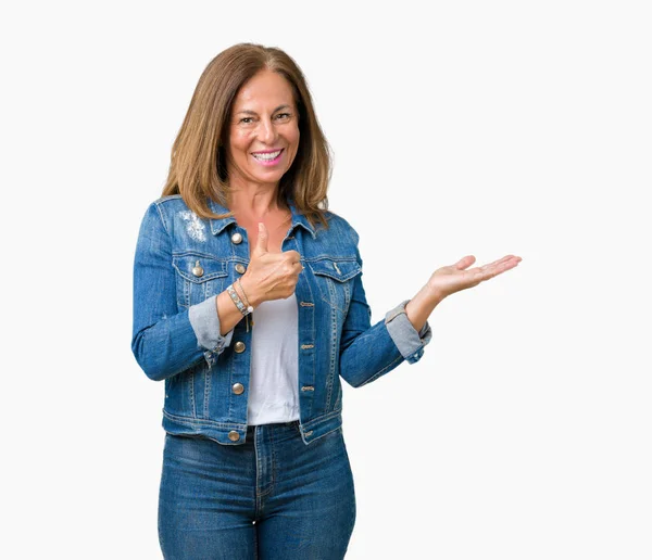 美しい中年女性にカジュアルなデニム ジャケットを着て分離背景幸せで陽気な笑みを浮かべて親指を示すパーム手でやって ジェスチャー — ストック写真