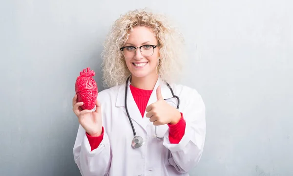 Jovem Cardiologista Loira Médico Mulher Sobre Grunge Parede Cinza Segurando — Fotografia de Stock
