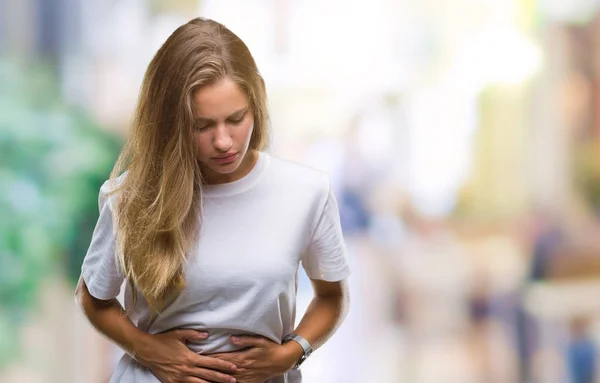 Young beautiful blonde woman wearing casual white t-shirt over isolated background with hand on stomach because nausea, painful disease feeling unwell. Ache concept.