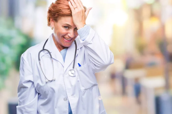 高级白种人医生妇女穿着医疗制服在孤立的背景惊讶与手在头上的错误 记住错误 糟糕的记忆概念 — 图库照片
