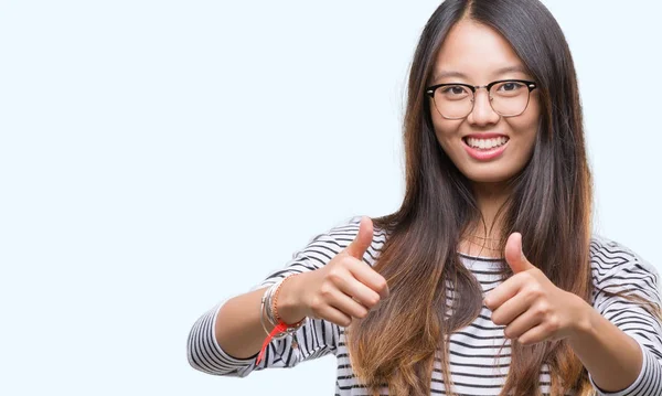 眼鏡をかけて孤立した背景の承認について若いアジア女性は笑顔と幸せな成功のため親指の手で肯定的なジェスチャーをしています カメラ 勝者のジェスチャーを見てください — ストック写真