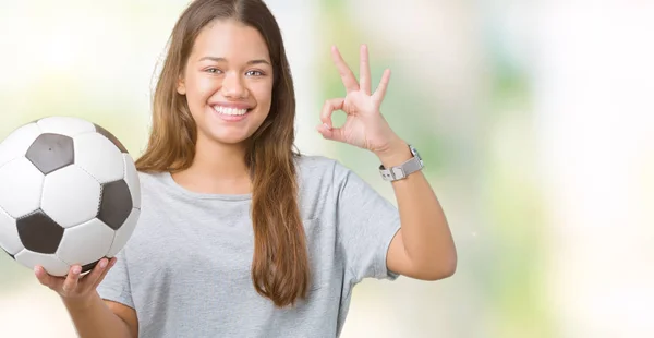 年轻美丽的黑发女子拿着足球在孤立的背景做确定的标志用手指 优秀的标志 — 图库照片