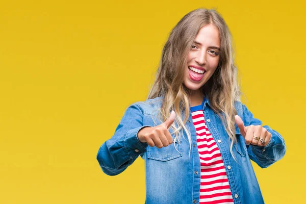 Beautiful young blonde woman over isolated background approving doing positive gesture with hand, thumbs up smiling and happy for success. Looking at the camera, winner gesture.