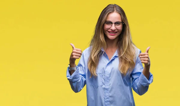 Young beautiful blonde business woman wearing glasses over isolated background success sign doing positive gesture with hand, thumbs up smiling and happy. Looking at the camera with cheerful expression, winner gesture.