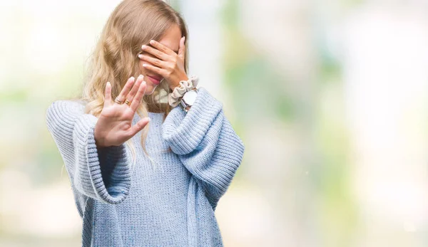 Beautiful young blonde woman wearing winter sweater over isolated background covering eyes with hands and doing stop gesture with sad and fear expression. Embarrassed and negative concept.