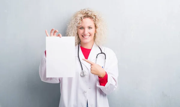 Jovem Mulher Médica Loira Sobre Grunge Parede Cinza Segurando Folha — Fotografia de Stock