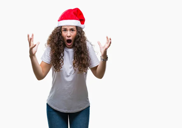 年轻的黑发女孩戴着圣诞帽在孤立的背景疯狂和疯狂的喊声和大喊大叫与侵略性的表情和手臂提出 挫折的概念 — 图库照片