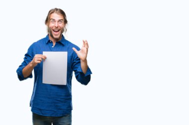 Çok mutlu ve heyecanlı, boş kağıt tutan izole arka plan büyük gülümseme ile çığlık ve ellerini kaldırdı kazanan ifade kutluyor zafer üzerinde uzun saçlı yakışıklı delikanlı