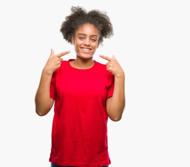 Kendinden emin gösterilen ve işaret parmakları diş ve ağız ile gülümseyen izole arka plan üzerinde genç afro Amerikalı kadın. Sağlık kavramı.