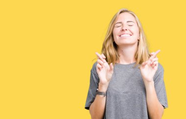 Umut ve gözleri kapalı geçiş parmaklarıyla gülümseyen izole arka plan üzerinde büyük boy rahat t-shirt giyen güzel ve genç birbayan. Şans ve batıl kavramı.