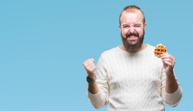 Genç beyaz hipster man üzerinde tatlı waffle yemek duygu tezahürat gurur çığlık ve zafer ve başarı çok heyecanlı, kutluyor arka plan izole