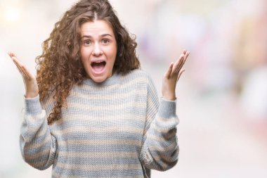 İzole arka plan üzerinde kutluyor kış kazak giyen genç kız şaşırttı ve silah ile başarı için hayran güzel esmer kıvırcık saçlı kaldırdı ve gözleri açık. Kazanan kavramı.