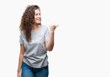 Casual göz seyir ve başparmak yanında yukarıyı mutlu yüz ile gülümseyen izole arka plan üzerinde giyen güzel genç esmer kıvırcık saçlı kız.