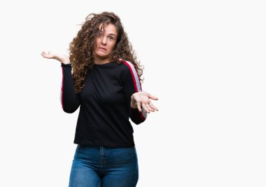 Casual göz izole arka plan clueless ve şaşkın bir ifadeyle kollar ve eller kaldırdı üzerinde giyen güzel genç esmer kıvırcık saçlı kız. Şüphe kavramı.