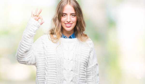 Beautiful young blonde woman wearing winter sweater over isolated background smiling positive doing ok sign with hand and fingers. Successful expression.