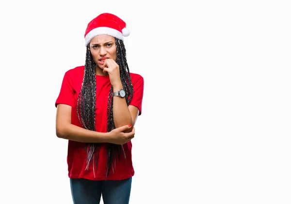 年轻的编织头发非洲裔美国女孩戴着圣诞帽在孤立的背景看起来紧张和紧张的手在嘴咬指甲 焦虑问题 — 图库照片