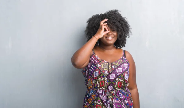年轻的非洲裔美国女人在灰色的格格墙上穿着五颜六色的衣服做确定的手势与手微笑 眼睛通过手指看着快乐的脸 — 图库照片